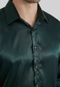 Chemise en satin vert foncé avec une texture lisse, col classique et six boutons assortis le long de la patte de boutonnage.