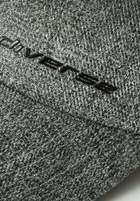 Szara czapka o strukturze materiału z wzorem w rybią łuskę, z czarnym logo "diverse" z przodu. Materiał wydaje się być trwały i tkany.