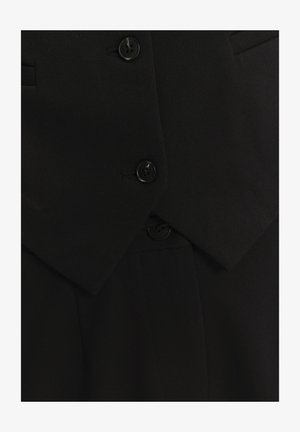 Zwarte op maat gemaakte blazer met een notch revers, dubbele sluiting, gestructureerde stof en vier zwarte knopen voor sluiting.