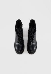 Zwarte leren enkelboots met een gestructureerde afwerking, voorzien van vetersluiting, bontvoering en zijritsen voor gemakkelijk aan- en uittrekken.