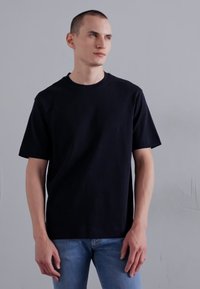 Camiseta preta de manga curta com gola redonda, feita de um tecido macio. O modelo combina-a com jeans azul claro. Design simples.
