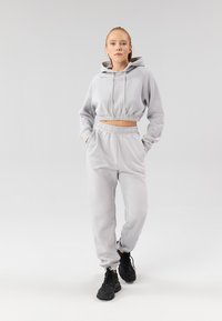 Ensemble sweat à capuche court gris clair et joggers assortis, avec bandes élastiques à la taille et aux poignets, en tissu doux, assorti à des baskets noires.