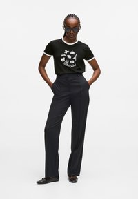 Czarna bawełniana koszulka z białymi wykończeniami i graficznymi nadrukami. Połączona z wysoko taliowanymi, ciemnymi spodniami i czarnymi płaskimi butami, charakteryzującymi się gładką fakturą.