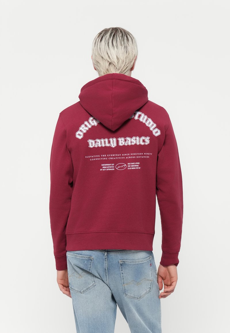 Sweat à capuche bordeaux avec un cordon de serrage, présentant un texte blanc au dos. Fabriqué en tissu texturé, avec des poignets et un ourlet côtelés.