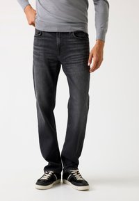Jeans negri din denim cu un croi lejer, având detalii de spălare decolorată și un design cu cinci buzunare, asortate cu adidași negri.