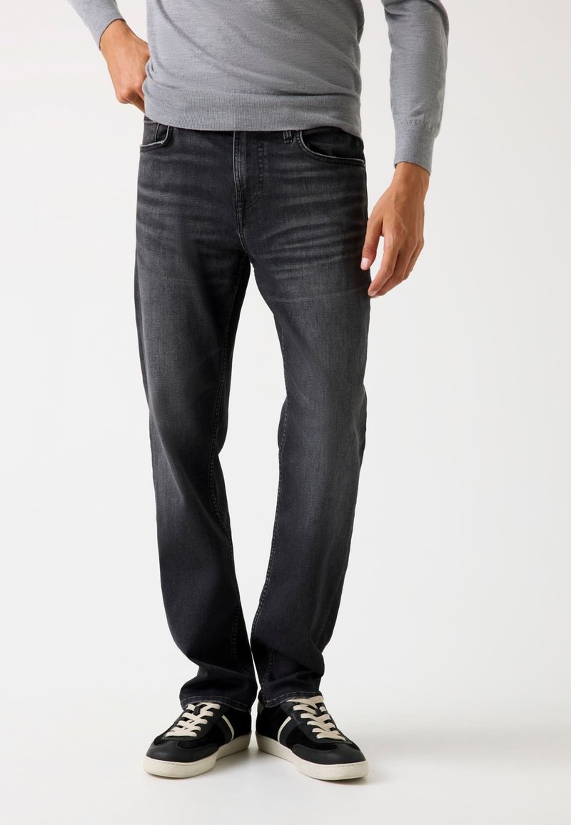 Jeans negri din denim cu un croi lejer, având detalii de spălare decolorată și un design cu cinci buzunare, asortate cu adidași negri.