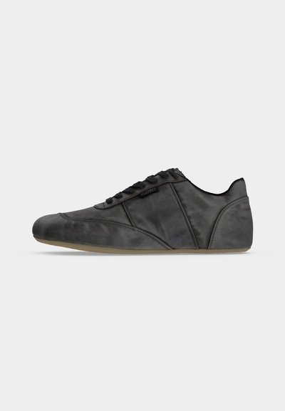 Μαύρο δερμάτινο χαμηλό sneaker με κορδόνια και ανοιχτό καφέ σόλα, απεικονίζεται σε προφίλ με απλό ανοιχτό γκρι φόντο.