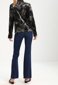 Black velvet top with floral pattern, long sleeves; paired with dark blue flared jeans. The outfit features a relaxed fit and plain black shoes.