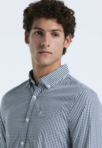 Marineblauwe en witte geblokte overhemdd met een kraag en zak. Gekenmerkt door een textiel van gekatoen en witte knopen.