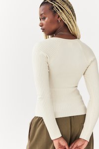 Haut à manches longues beige à côtes, avec un design ajusté, présentant des côtes contrastées sur les manches et un corps lisse. Matière en tricot texturée.