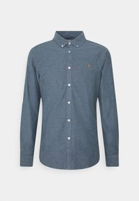 Chemise homme à manches longues à boutons en tissu chambray bleu avec col boutonné et petit logo jaune brodé sur la poitrine.