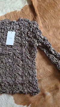Blusa taupe de mangas longas com franzidos, com etiqueta a dizer "YAS", disposta sobre uma superfície de pele texturizada em castanho e branco.