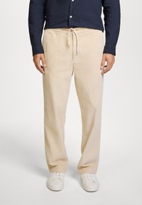 Pantalones de pana beige con costuras verticales, cintura con cordón y bolsillos laterales, combinados con zapatillas blancas. Adecuados para un estilo casual.