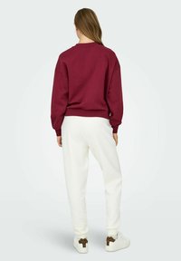 Burgundy sweatshirt with dropped shoulders, paired with white sweatpants and white sneakers featuring leopard print accents on the heels.