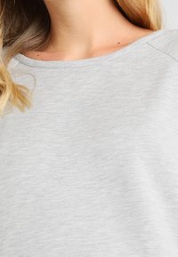 Top de manga corta de color gris claro hecho de tela suave. Presenta un cuello redondo ancho y una textura lisa, con un ajuste relajado y detalles mínimos de costuras.