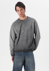 Kuldgrå sweatshirt med et tekstureret ørnedesign i midten, med rund halsudskæring og ribbede manchetter og nederdel.