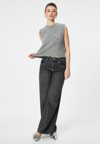 Grauer, gestrickter ärmelloser Pullover mit Zopfmuster, kombiniert mit hoch taillierten, schwarzen, weiten Jeans und silbernen flachen Schuhen.