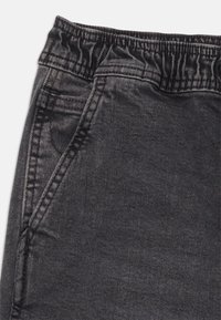 Joggers de mezclilla negra con cintura elástica, bolsillos laterales y un discreto detallado de costuras, con un acabado suave y texturizado.