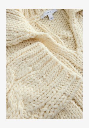 Chunky creamfarvet strikket cardigan med sjalskrave og teksturerede mønstre. Stoffet er tykt med et blødt, fluffy udseende.
