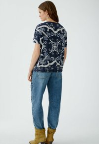 Haut à motifs bleu marine avec des manches courtes et un col rond, arborant un design abstrait blanc. Porté avec un jean bleu et des bottes jaunes.