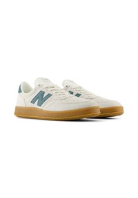 Zapatillas de ante blancas con acentos en azul verdoso y suela de goma. Presentan una puntera perforada y un diseño clásico de cordones.