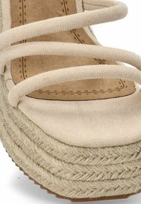 Sandalia de plataforma beige con correas suaves tipo gamuza, detalle de yute trenzado en la suela elevada y una plantilla acolchada en tono marrón.