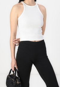 Un top court à col halter blanc à côtes associé à un legging noir taille haute, avec un petit sac à main noir texturé orné de quincaillerie dorée.