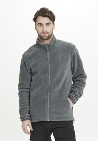Giacca in pile grigia con zip frontale, colletto alto e tasche laterali. Presenta un tessuto testurizzato e un logo discreto sul petto.