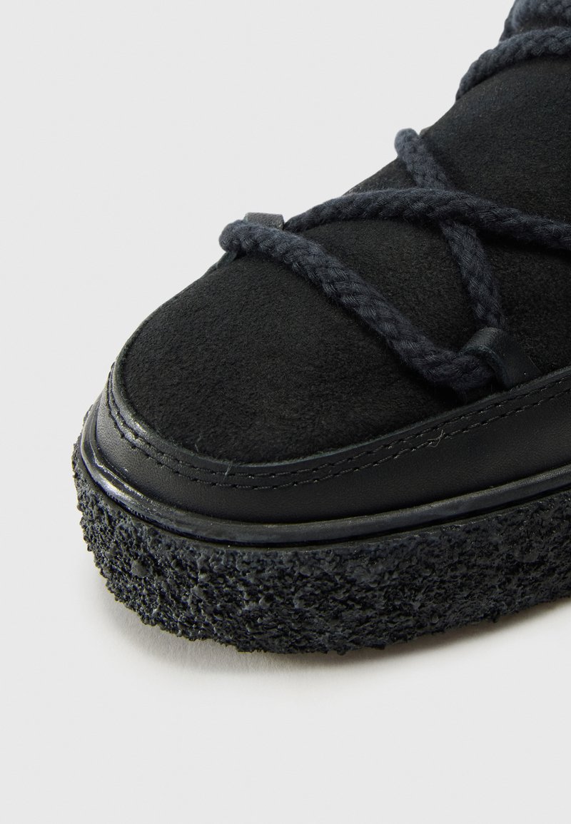 Czarne trampki z zamszową cholewką, teksturowaną gumową podeszwą i plecionymi sznurówkami, z gładkim skórzanym wykończeniem wokół kostki.