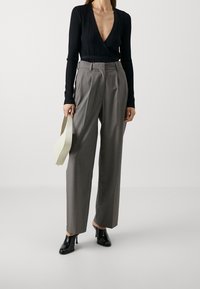 Svart ribbad långärmad topp kombinerad med högmidjade grå byxor. Modellen bär svarta klackskor och håller en ljusfärgad handväska.