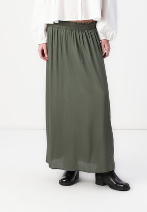 Jupe maxi vert olive avec une taille élastique, fabriquée en tissu fluide. Associée avec des bottines noires et un blouson blanc court.