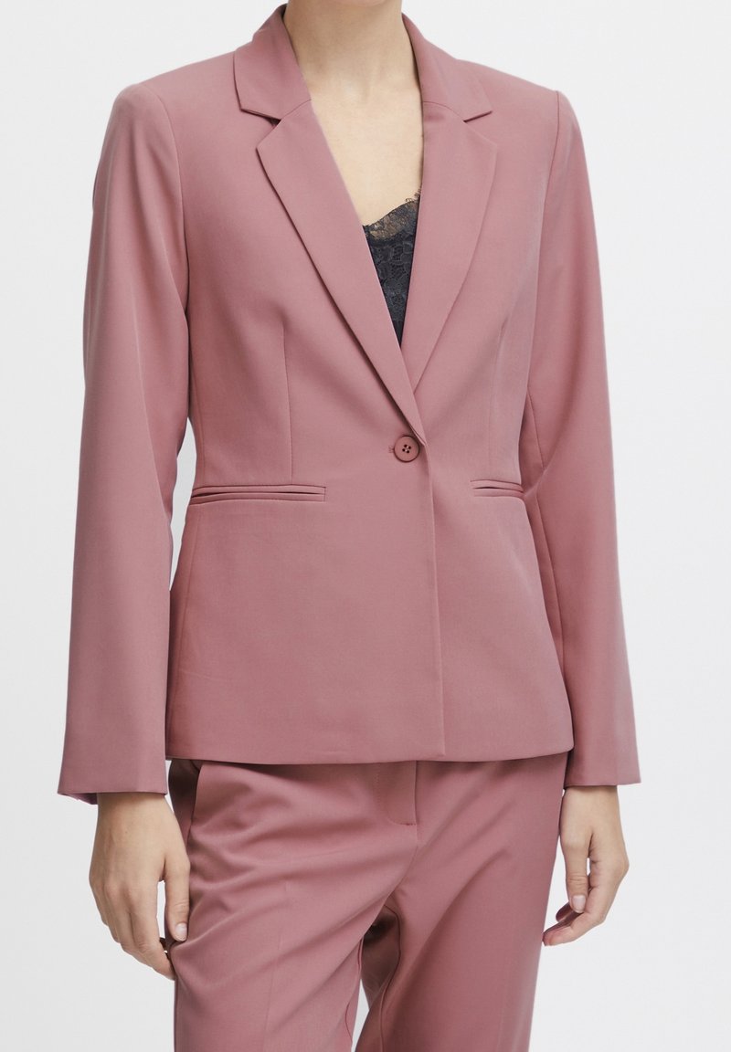 Ruusuinen bleiseri, jossa on yksittäinen nappi, muotoillut kaulukset ja etutaskut, valmistettu sileästä, kevyestä kankaasta. Yhdistetty samansävyisiin housuihin.