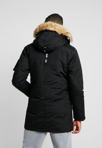 Zwarte parka-jack met een met bont gevoerde capuchon, voorzien van een ritssluiting en zijzakken. De stof lijkt textuur te hebben en is geïsoleerd voor warmte.