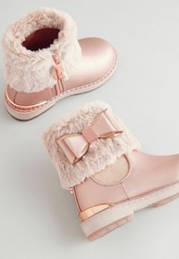 Rosa Kunstleder-Stiefeletten mit einem flauschigen Schaft, einer Schleifenakzent und roségoldenen Beschlägen. Sie verfügen über eine strukturierte Sohle und einen seitlichen Reißverschluss.