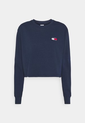 Sudadera recortada de color azul marino en tejido suave con mangas largas. Presenta un pequeño parche de logo "TOMMY JEANS" multicolor en el lado izquierdo del pecho.