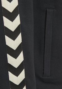 Tessuto nero con una striscia a zig-zag bianca e nera testurizzata. Include una tasca laterale con una finitura semplice e liscia.
