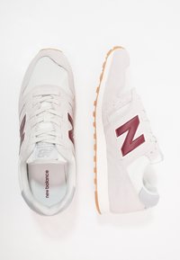 Baskets athlétiques gris clair en suède et mesh, avec un logo bordeaux, des accents blancs, et une semelle en caoutchouc texturée.