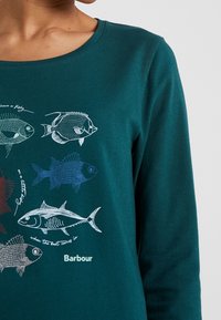 Türkisfarbenes Langarmshirt mit verschiedenen Fischillustrationen in Weiß und Rot, mit der Marke "Barbour" gedruckt am unteren Ende.