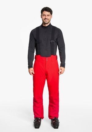 Red ski pants with adjustable black suspenders, buttoned waist, and a sleek design. Paired with black ski boots for winter sports.
