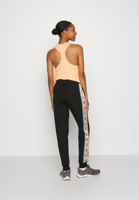Débardeur sportif orange avec un dos nageur, associé à un jogging noir présentant un motif de rayure latérale contrastante et des poignets côtelés.
