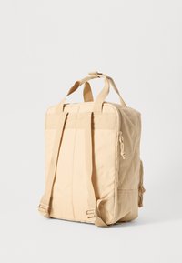 Beige ryggsäck med rektangulär form, gjord av ett hållbart tyg. Har dubbla handtag upptill och justerbara remmar, samt en sidoficka med dragkedja.