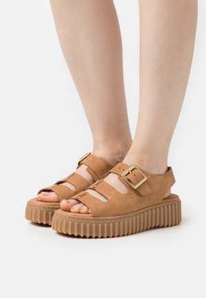 Brown leather platform sandals with cut-out design, adjustable buckle, and ridged rubber sole. Open-toe style showcasing toes.