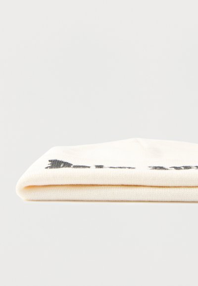 Διπλωμένο κρεμ ύφασμα με μερικώς ορατό μαύρο κείμενο ή σχέδιο στην κορυφή, τοποθετημένο πάνω σε απλό ανοιχτό φόντο.