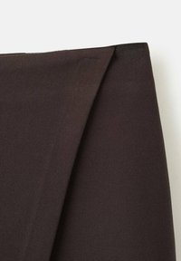 Prim-plan al unei țesături maro închis cu o pliură ascuțită și înclinată pe un fundal deschis, evidențiind textura și liniile clare.