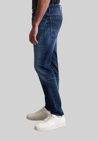 Donkerblauwe denim jeans met een slim fit, featuring een vervaagde wasbeurt, achterzakken en een recht model, gecombineerd met witte sneakers.