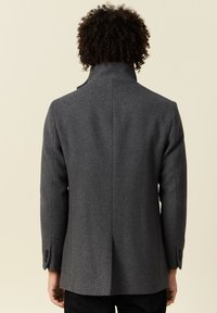 Cappotto grigio in misto lana con colletto alto, forma aderente e spacco singolo. Presenta quattro bottoni su ciascun polsino, offrendo un aspetto elegante e sartoriale.