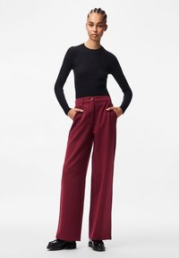 Mustaga sooniga pikad varrukad, koos laia lõikega tumepunaste pükstega, millel onTaskud ja nööpide detail, kantud mustade kingadega.