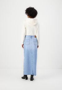 Light blue denim maxi skirt with side slit, worn over a cream hoodie. Features two back pockets and a belt loop. Footwear is black, chunky-heeled boots.