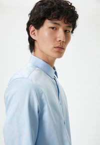 Ljusblå skjorta med knapp-up, strukturerad krage, mjuk bomullstextur och slim fit-design. Har en hel knappstängning.
