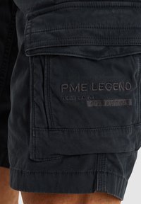 Crne cargo kratke hlače izrađene od izdržljive tkanine, s više džepova, prošivenim detaljima i reljefnom oznakom s boka.